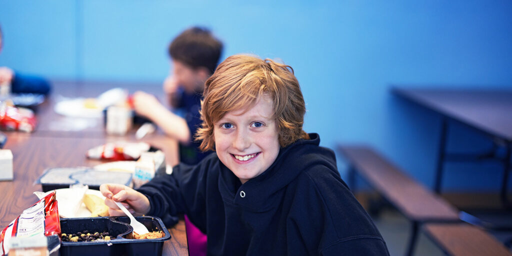 Smiling student eating lunch in cafeteria.